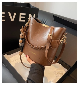 Detail of brown bucket bag with vintage texture, braided strap, and rabbit charm