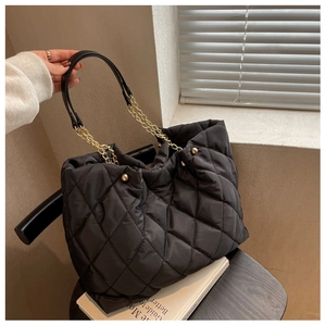 Detail of black quilted nylon tote bag featuring gold chain straps and rhombic stitching