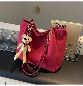 Detail of rose red canvas tote bag with gold chain strap and cute bear charm decor