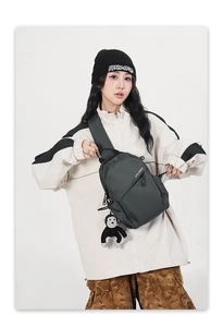 Detail of charcoal grey waterproof nylon chest bag with monkey plush pendant and logo