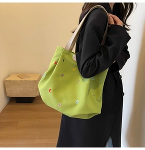 Detail of vibrant green canvas tote bag featuring colorful embroidered letters and cream straps