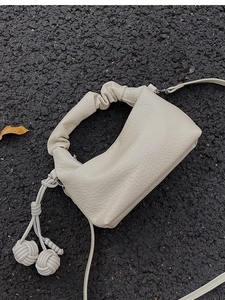 Détail du sac en cuir crème avec anse froncée et breloques boules tressées chic