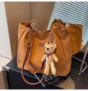 Detail of textured brown tote bag with leather straps, gold chain and bear charm