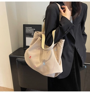 Detailed shot of beige canvas tote bag with embroidered letters on black blazer