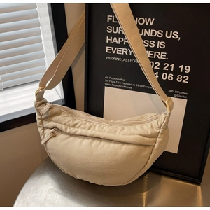 Detail view of a beige nylon crescent crossbody bag showing double zippers and wide strap