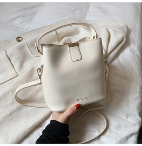 Detail of cream bucket bag with brand embossing, gold hardware and leather strap