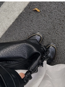 Détail d'un sac en cuir noir grainé avec une poignée distinctive à gros nœuds tressés