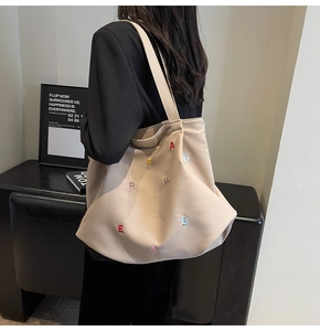 Detail of beige canvas tote bag with colorful letter embroidery and wide shoulder strap