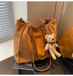 Detail of caramel canvas tote bag with leather straps, gold chain, and bear charm