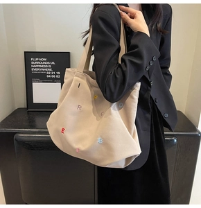 Detail of cream canvas tote bag featuring colorful embroidered letters and sturdy shoulder strap