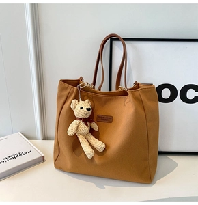Close-up of brown canvas tote bag featuring a leather logo tag and cute bear pendant