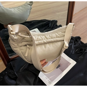 Detail of beige nylon crescent bag featuring adjustable wide strap and quilted texture