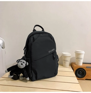 Detail of black nylon crossbody bag with STLANGS logo and plush monkey charm on desk