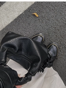 Détail de la texture en cuir plissé noir d'un sac à main avec des bottes Dr. Martens
