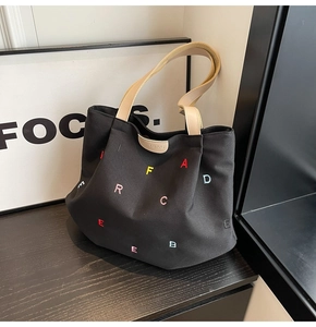 Detail of colorful embroidered letters and brand leather patch on black canvas tote bag