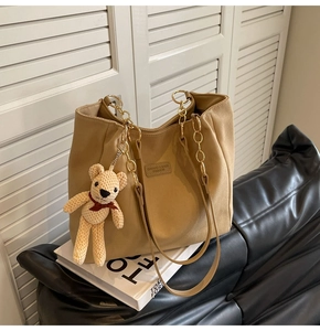 Detail of khaki canvas tote bag with chain strap, logo patch and cute bear charm