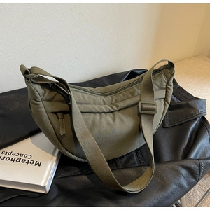 Detail of army green nylon crescent bag with adjustable strap on leather background