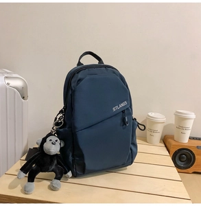 Detail of blue crossbody bag with STLANGS logo and plush monkey charm on wooden tray