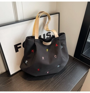 Detail of black canvas tote bag showing colorful embroidered letters and brand leather patch