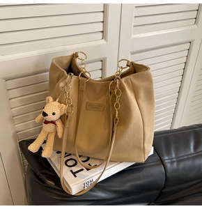 Macro view of khaki canvas tote with metal chain straps and plush bear ornament detail