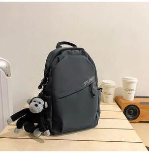 Detailed close-up of a dark grey nylon backpack with a plush gorilla keychain on a table