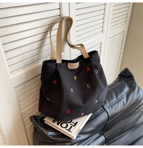 Close-up of black canvas tote bag featuring colorful embroidery and leather logo detail