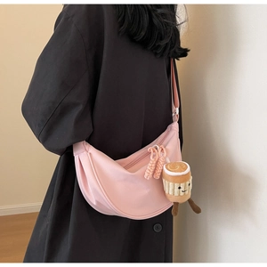 Detail view of a pink nylon crescent bag with a cute plush charm on a black coat