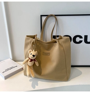 Close-up of khaki canvas tote bag with leather label and cute bear charm decoration