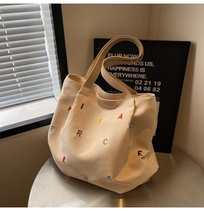 Detail view of beige canvas tote bag with multi-colored embroidered letters and leather label