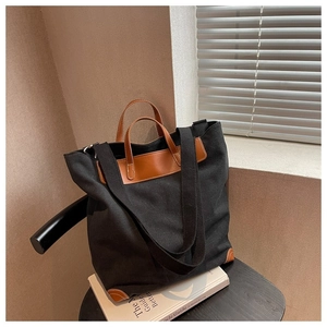 Detalle de bolso tote de lona con asas de cuero marrón y correa de hombro negra ancha