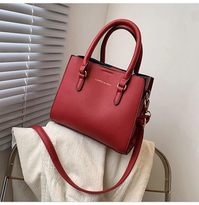 Detail of red leather bridal handbag with golden logo and refined litchi grain texture