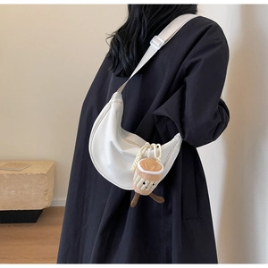 Detailed view of a white nylon crescent bag with wide strap and plush coffee cup charm