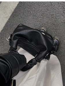 Détail du sac en cuir noir avec poignée plissée et fermeture éclair sur le dessus