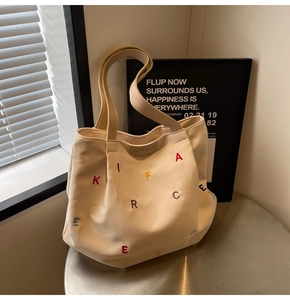 Detailed close-up of embroidered colorful letters on a cream canvas tote bag with leather tag