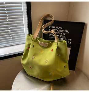 Detail of lime green canvas tote bag with colorful letter embroidery and leather logo tag