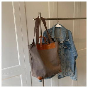 Detalle del bolso tote de lona café con ribete de cuero marrón y asas de hombro