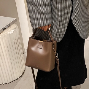 Chic coffee brown bucket bag with gold clasp and adjustable strap shown on model