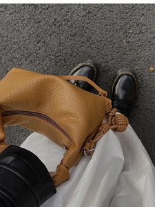 Détail d'un sac à main marron en cuir grainé avec de grands nœuds tressés décoratifs