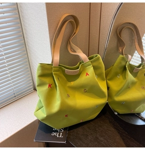 Close-up of grass green canvas tote bag featuring colorful embroidery and leather logo tag
