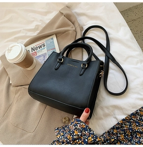 Detail of black litchi grain leather handbag with gold metal hardware on white bedding
