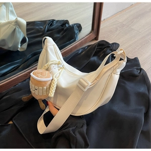 Close-up of white crescent nylon bag with wide strap and cute plush charm detail