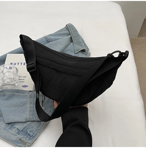 Close-up of black nylon crescent crossbody bag with zipper on blue denim jacket