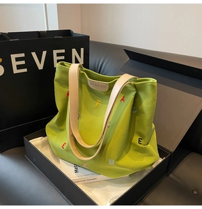 Close-up of colorful letter embroidery and leather logo on light green canvas tote bag