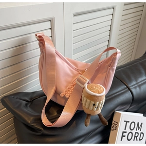 Detail of pink nylon crescent bag with wide strap and cute plush charm on leather sofa