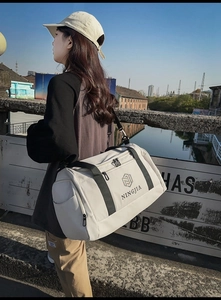 Outdoor model holding off-white nylon travel bag with black shoulder strap and side pockets