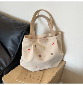 Detailed shot of cream canvas tote bag with colorful embroidery on a stone pedestal