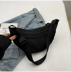 Detail of black quilted nylon crescent bag with adjustable strap on denim jacket