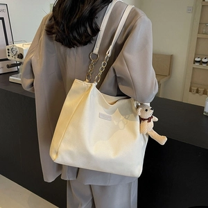 Off-white canvas tote bag with chain strap and teddy bear charm on model shoulder