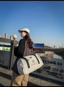 Outdoor lifestyle shot of a large nylon travel bag in beige with a black shoulder strap
