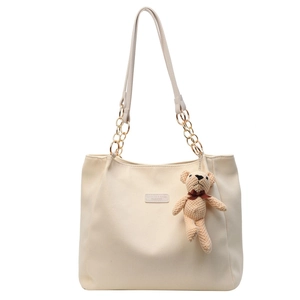 Cream canvas tote bag with gold chain strap and plush bear pendant on white background